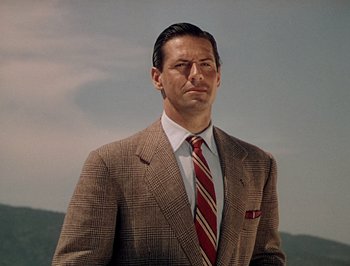 Movie still from “Pandora and the Flying Dutchman” (1951), directed by Albert Lewin – A man in a suit and tie standing in front of a sky background; Close Up shot, Low angle