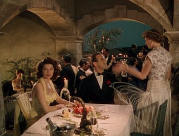 Movie still from “Pandora and the Flying Dutchman” (1951), directed by Albert Lewin – A group of people sitting at a table with wine glasses; Wide shot, Over the shoulder angle