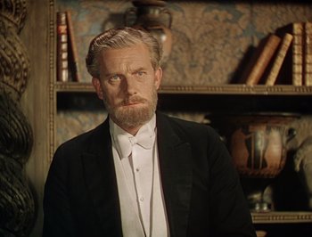 Movie still from “Pandora and the Flying Dutchman” (1951), directed by Albert Lewin – An older man wearing a tuxedo in front of bookshelves; Medium shot, Low angle
