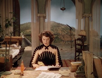 Movie still from “Pandora and the Flying Dutchman” (1951), directed by Albert Lewin – A woman sitting at a table reading a book; Medium shot, High angle