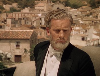 Movie still from “Pandora and the Flying Dutchman” (1951), directed by Albert Lewin – A man in a tuxedo sitting in a chair in front of some buildings; Medium shot, Low angle