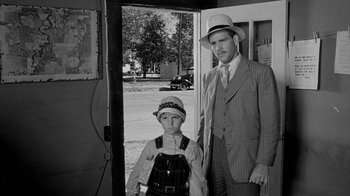 Movie still from “Paper Moon” (1973), directed by Peter Bogdanovich – A man and a boy standing next to each other in front of a building; Medium shot, Over the shoulder angle