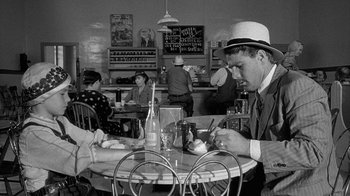 Movie still from “Paper Moon” (1973), directed by Peter Bogdanovich – A man sitting at a table in front of a bottle of soda; Medium shot, High angle
