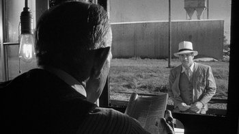 Movie still from “Paper Moon” (1973), directed by Peter Bogdanovich – A man sitting in front of another man reading a newspaper; Medium shot, Over the shoulder angle