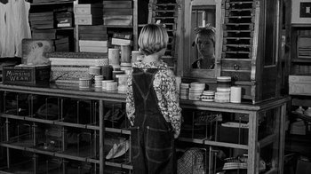 Movie still from “Paper Moon” (1973), directed by Peter Bogdanovich – A woman standing in front of a mirror in a store; Medium shot, Over the shoulder angle