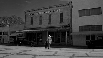 Movie still from “Paper Moon” (1973), directed by Peter Bogdanovich – A man walking down the street holding a bag; Wide shot, High angle