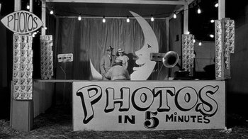 Movie still from “Paper Moon” (1973), directed by Peter Bogdanovich – Two men are sitting on a stage with a microphone in front of them; Wide shot, High angle