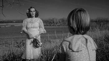 Movie still from “Paper Moon” (1973), directed by Peter Bogdanovich – A woman in a white dress holding a banana in a field; Medium shot, Over the shoulder angle