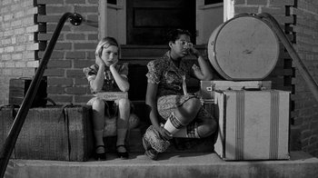 Movie still from “Paper Moon” (1973), directed by Peter Bogdanovich – A woman and a girl sitting on a porch with suitcases; Medium shot, High angle