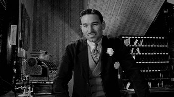 Movie still from “Paper Moon” (1973), directed by Peter Bogdanovich – A man in a suit standing in front of a desk; Medium shot, Low angle