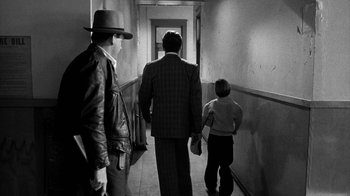 Movie still from “Paper Moon” (1973), directed by Peter Bogdanovich – A man and a boy walk down a hallway with a man wearing a hat; Wide shot, Over the shoulder angle