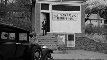 Movie still from “Paper Moon” (1973), directed by Peter Bogdanovich – An old photo of a man standing in front of a sheriff's department; Extreme Wide shot, Low angle