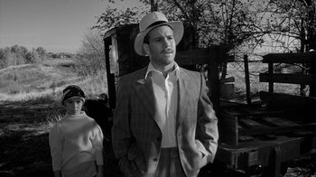 Movie still from “Paper Moon” (1973), directed by Peter Bogdanovich – A man wearing a suit and a hat standing next to a woman; Medium shot, Low angle