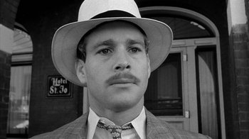 Movie still from “Paper Moon” (1973), directed by Peter Bogdanovich – A black and white photo of a man wearing a suit and a hat; Close Up shot, Over the shoulder angle
