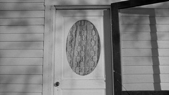 Movie still from “Paper Moon” (1973), directed by Peter Bogdanovich – An oval window in a white door with a lace curtain; Medium shot, High angle