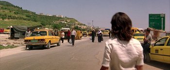 Movie still from “Paradise Now” (2005), directed by Hany Abu-Assad – A group of people walking down a street near some cars; Wide shot, Over the shoulder angle