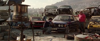 Movie still from “Paradise Now” (2005), directed by Hany Abu-Assad – A man working on a car in the middle of a pile of cars; Wide shot, High angle
