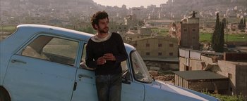Movie still from “Paradise Now” (2005), directed by Hany Abu-Assad – A man standing next to an old car in a city; Medium shot, Over the shoulder angle