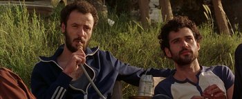Movie still from “Paradise Now” (2005), directed by Hany Abu-Assad – A man sitting next to another man holding a wire; Medium shot, Low angle