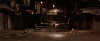 Movie still from “Paradise Now” (2005), directed by Hany Abu-Assad – A person walking on a street at night; Extreme Wide shot, High angle