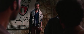 Movie still from “Paradise Now” (2005), directed by Hany Abu-Assad – A man with a scarf around his neck is standing in front of a brick wall; Medium shot, Over the shoulder angle