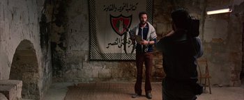 Movie still from “Paradise Now” (2005), directed by Hany Abu-Assad – A man standing in front of a wall holding a laptop; Wide shot, Over the shoulder angle