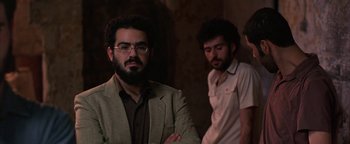 Movie still from “Paradise Now” (2005), directed by Hany Abu-Assad – A man with a beard wearing glasses and a suit; Medium shot, Over the shoulder angle