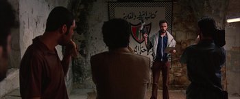 Movie still from “Paradise Now” (2005), directed by Hany Abu-Assad – A man standing in front of two other men; Wide shot, Over the shoulder angle