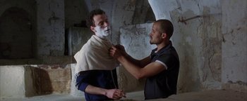 Movie still from “Paradise Now” (2005), directed by Hany Abu-Assad – A man shaving another man's face with a towel around his neck; Medium shot, Over the shoulder angle