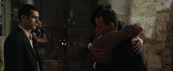 Movie still from “Paradise Now” (2005), directed by Hany Abu-Assad – A man hugging another man in a dark room; Medium shot, Over the shoulder angle