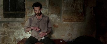 Movie still from “Paradise Now” (2005), directed by Hany Abu-Assad – A man sitting on the ground holding something in his hand; Medium shot, High angle