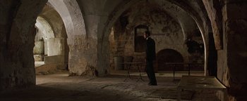 Movie still from “Paradise Now” (2005), directed by Hany Abu-Assad – A man standing in an old building with a table; Wide shot, High angle