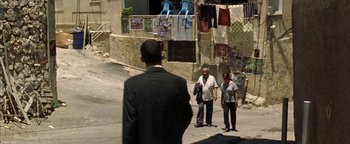 Movie still from “Paradise Now” (2005), directed by Hany Abu-Assad – A man in a suit and tie standing on a sidewalk; Wide shot, Over the shoulder angle