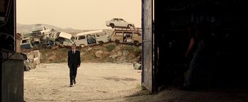 Movie still from “Paradise Now” (2005), directed by Hany Abu-Assad – A man in a suit walking in front of a pile of cars; Extreme Wide shot, Low angle