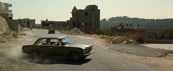 Movie still from “Paradise Now” (2005), directed by Hany Abu-Assad – A car driving down a street past a building; Extreme Wide shot, Low angle