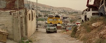 Movie still from “Paradise Now” (2005), directed by Hany Abu-Assad – A car parked on the side of the road next to a building; Extreme Wide shot, High angle
