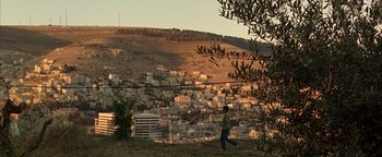 Movie still from “Paradise Now” (2005), directed by Hany Abu-Assad – A person walking on top of a hill near a city; Extreme Wide shot, High angle