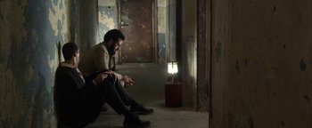 Movie still from “Paradise Now” (2005), directed by Hany Abu-Assad – A man sitting on the ground next to a lamp; Medium shot, Over the shoulder angle