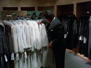 Movie still from “Paris Is Burning” (1990), directed by Jennie Livingston – A man in a black suit looking at fur coats; Medium shot, Overhead angle
