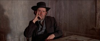 Movie still from “Pat Garrett & Billy the Kid” (1973), directed by Sam Peckinpah – A man wearing a suit and hat sitting at a wooden table; Close Up shot, Low angle
