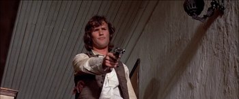 Movie still from “Pat Garrett & Billy the Kid” (1973), directed by Sam Peckinpah – A man holding a gun while standing in front of a wall; Medium shot, Low angle