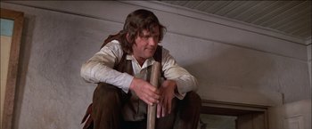Movie still from “Pat Garrett & Billy the Kid” (1973), directed by Sam Peckinpah – A man sitting on the ground holding a wooden stick; Medium shot, Low angle