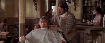 Movie still from “Pat Garrett & Billy the Kid” (1973), directed by Sam Peckinpah – A man getting his hair cut by another man; Medium shot, Over the shoulder angle
