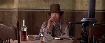 Movie still from “Pat Garrett & Billy the Kid” (1973), directed by Sam Peckinpah – A man sitting at a table with a drink in his hand; Medium shot, Low angle