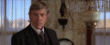 Movie still from “Pat Garrett & Billy the Kid” (1973), directed by Sam Peckinpah – An older man wearing a suit and tie in front of a clock; Close Up shot, Over the shoulder angle