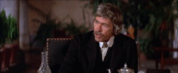 Movie still from “Pat Garrett & Billy the Kid” (1973), directed by Sam Peckinpah – An older man wearing a suit and tie sitting at a table; Close Up shot, Over the shoulder angle