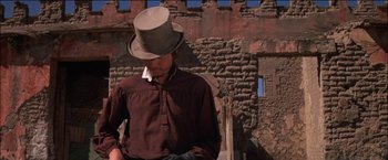 Movie still from “Pat Garrett & Billy the Kid” (1973), directed by Sam Peckinpah – A man wearing a top hat standing in front of a brick building; Medium shot, Low angle