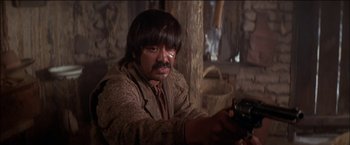 Movie still from “Pat Garrett & Billy the Kid” (1973), directed by Sam Peckinpah – A man with long black hair holding a gun; Close Up shot, Over the shoulder angle