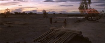 Movie still from “Pat Garrett & Billy the Kid” (1973), directed by Sam Peckinpah – Two people standing in a field near a body of water; Extreme Wide shot, Over the shoulder angle