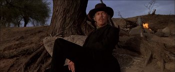 Movie still from “Pat Garrett & Billy the Kid” (1973), directed by Sam Peckinpah – A man sitting on a rock near a tree; Medium shot, Low angle